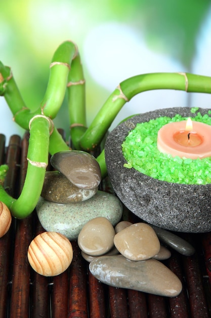 Bodegón con planta de bambú verde y piedras sobre estera de bambú sobre fondo brillante