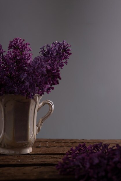 Bodegón de ramas lilas en una taza de té sobre una mesa de madera sobre un fondo gris Bodegón de primavera en una llave oscura