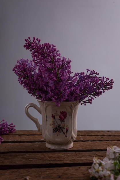 Bodegón de ramas lilas en una taza de té sobre una mesa de madera sobre un fondo gris Bodegón de primavera en una llave oscura