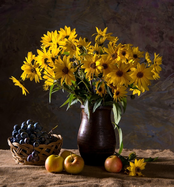 Bodegón con ramo de flores amarillas (rudbeckia) en jarrón marrón y frutas