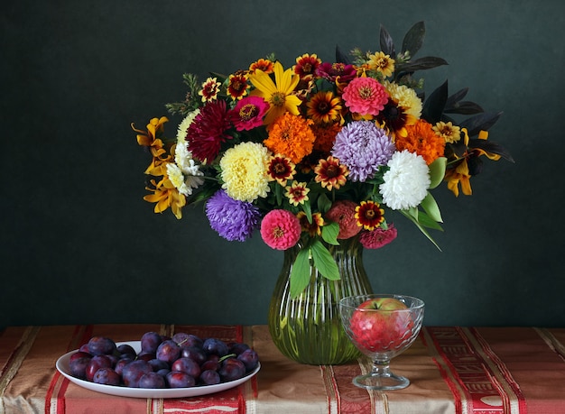 Bodegón con un ramo de flores de otoño, manzanas y ciruelas.