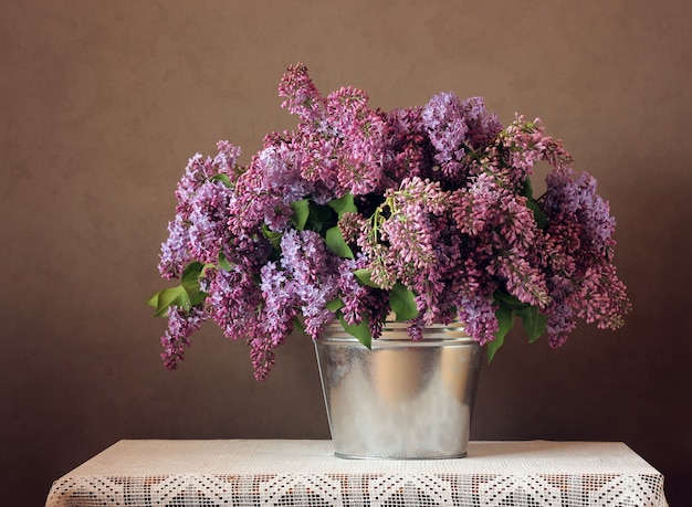 Bodegón con un ramo de lilas en un cubo.