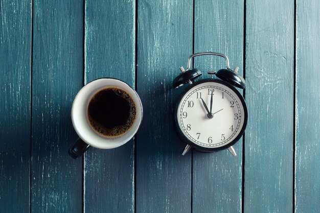 Bodegón con reloj despertador y taza de café en la mesa de madera