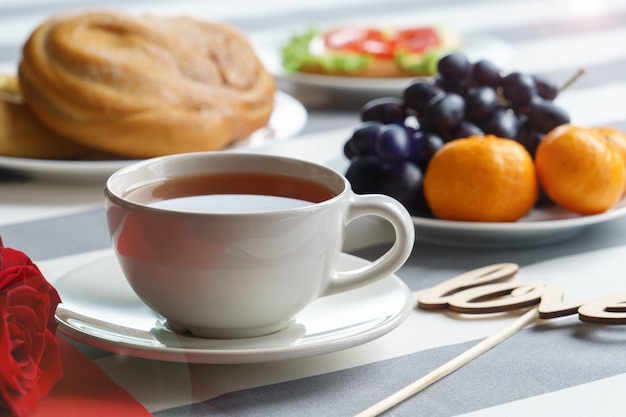 Bodegón romántico con una taza de té y atributos de vacaciones de color rojo brillante.