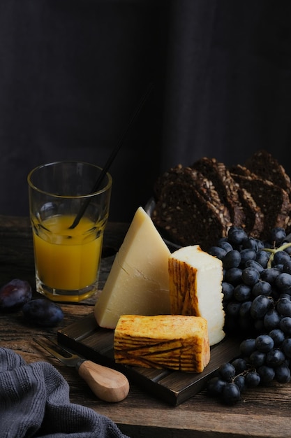 Bodegón de surtido de platos de queso. Frutas, cuchillo y nueces con diferentes quesos sobre tabla de madera.