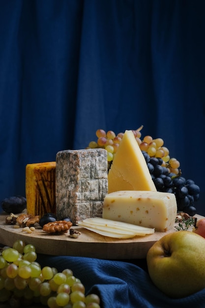 Bodegón de surtido de platos de queso. Frutas, cuchillo y nueces con diferentes quesos sobre tabla de madera.