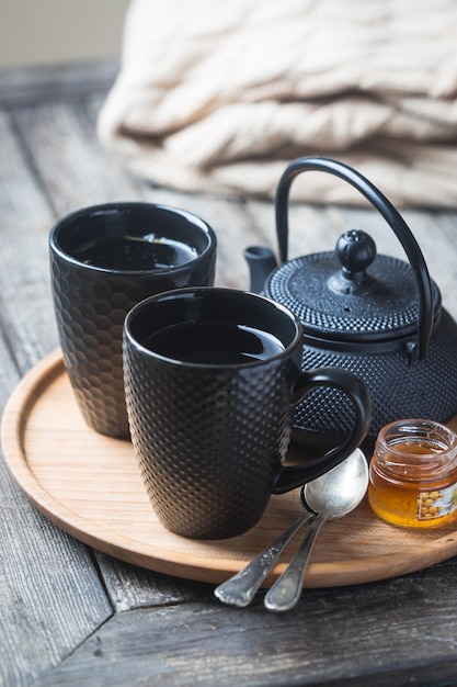 Bodegón de taza de té negro con tetera en una bandeja sobre la mesa de madera. Hora del té en un ambiente acogedor.