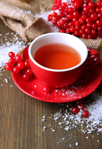 Bodegón con té viburnum en taza, bayas y nieve, sobre servilleta de cilicio