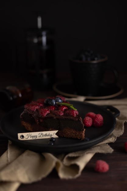 Bodegón con un trozo de pastel de brownie de chocolate con frambuesas Inscripción de feliz cumpleaños