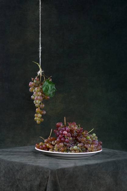 Bodegón con uvas en un plato y un racimo en una cuerda.