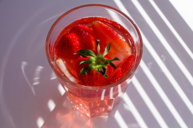 Bodegón con vaso de refrescante sangría de fresa con vino espumoso, fresa, cubitos de hielo