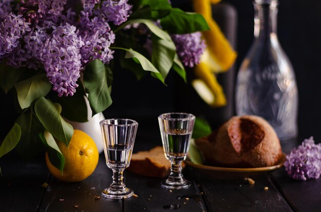 Bodegón con vasos de vodka ramo de lilas decantador larga exposición profundidad de campo