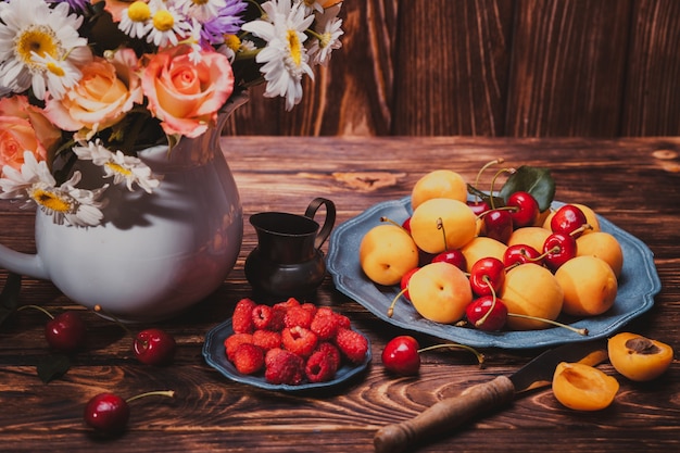 Bodegón de verano con melocotones, frambuesas, cerezas y flores en una mesa de madera