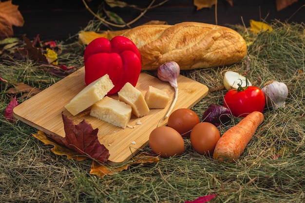 Foto bodegón con verduras y queso en una tabla para cortar en el heno