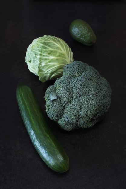 Bodegón con verduras verdes brócoli repollo pepino y aguacate sobre un fondo oscuro