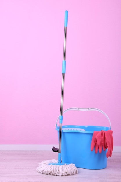 Bodenwischer und Eimer zum Waschen im Zimmer auf rosafarbenem Wandhintergrund