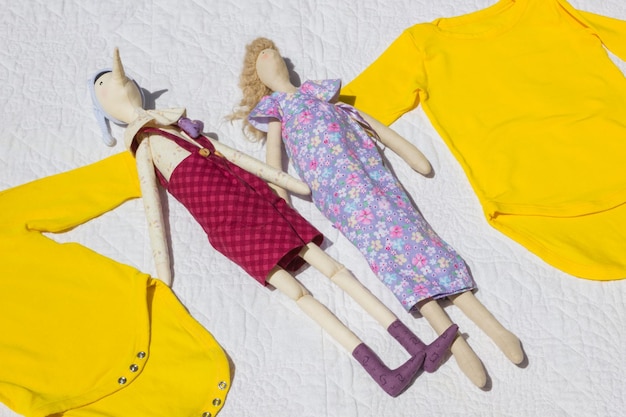 Body amarelo bebê roupas de bebê e bonecas no pano branco Roupas para bebês jaqueta amarela tamanho pequeno para venda Bonecas artesanais para crianças