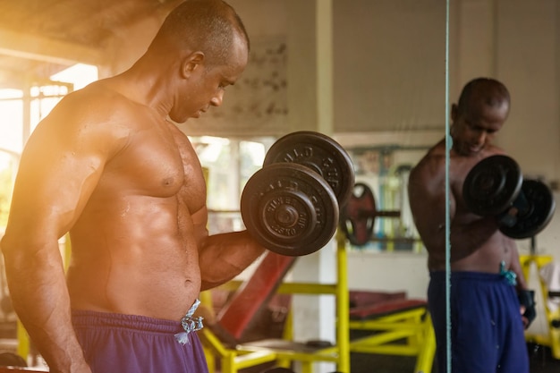 Bodybuilder aus Sri Lanka, der im Spiegel Hanteln hebt Sportler, der Übungen mit Hanteln im alten Fitnessstudio macht