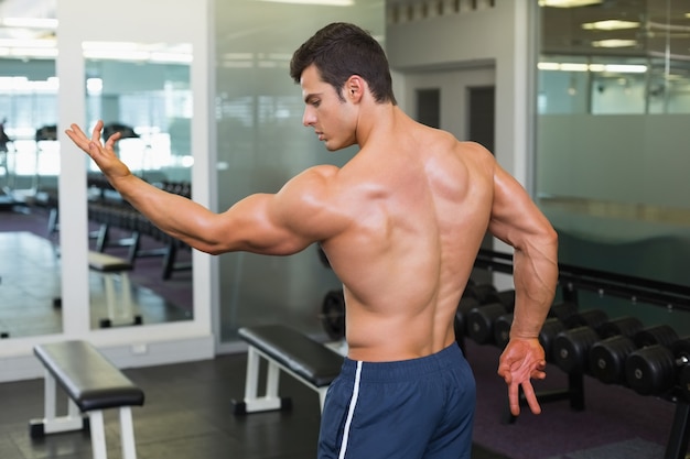 Bodybuilder sin camisa posando en el gimnasio