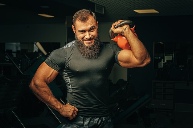 Bodybuilder, der Übungen mit Hanteln in einem dunklen Fitnessstudio macht