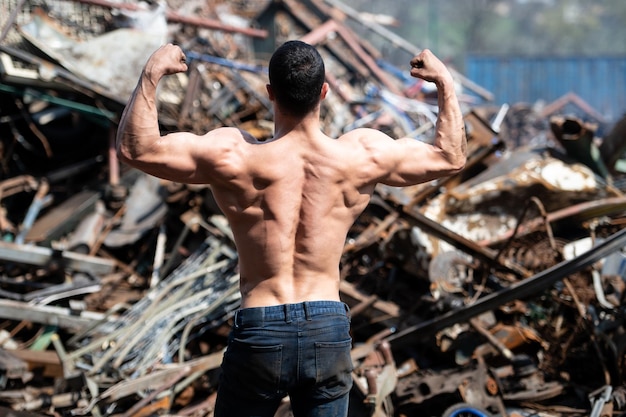 Bodybuilder lässt seine Muskeln im Freien auf einem industriellen Schrottplatz spielen