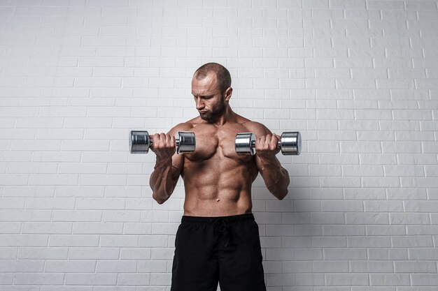 Foto bodybuilder macht übungen für bizeps mit einer hantel gegen mauer.