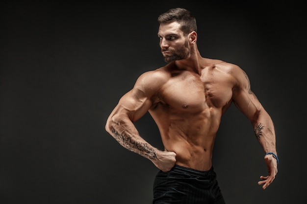 Bodybuilder posieren. Mann mit Muskeln auf dunkler Wand der Eignung.