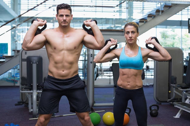 Bodybuilding homem e mulher levantando kettlebells olhando câmera