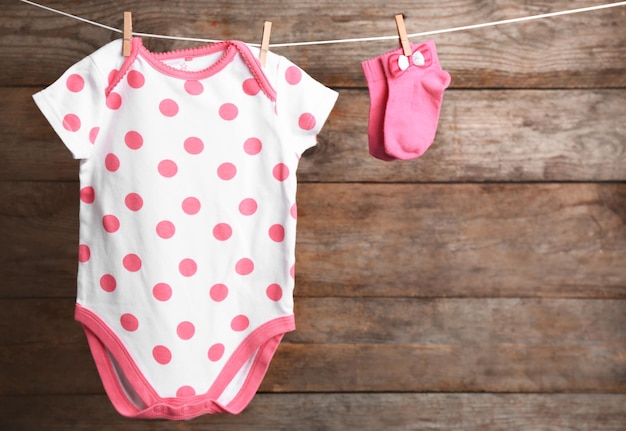 Bodysuit und Socken auf Wäscheleine vor Holzhintergrund Platz für Text Babyzubehör