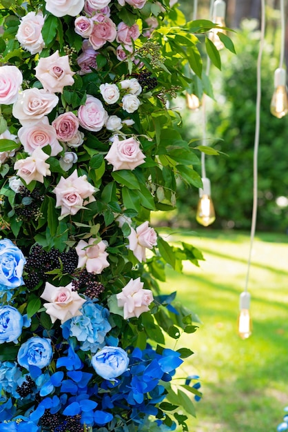 Bogen für eine Hochzeitszeremonie mit frischen Blumen in Weiß und Rosa und Blau und Glühbirnen, Nahaufnahme. Hochzeitsdekorationen. Weicher selektiver Fokus.