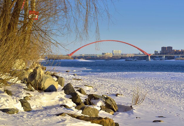 Bogenbrücke am Fluss Ob Bugrinsky-Brücke an einem felsigen, schneebedeckten Ufer in einer Großstadt im Frühjahr