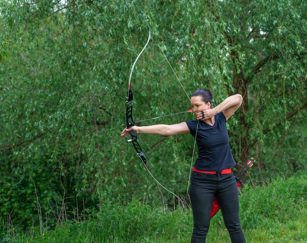 Foto bogenschießen in der natur. eine junge attraktive frau trainiert in einem bogenschuss mit einem pfeil auf ein ziel im wald