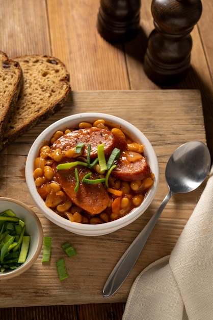 Bohnen mit Wurst und Tomatensauce in Schüssel Bohneneintopf hausgemachtes rustikales englisches Essen Rustikaler Holzhintergrund