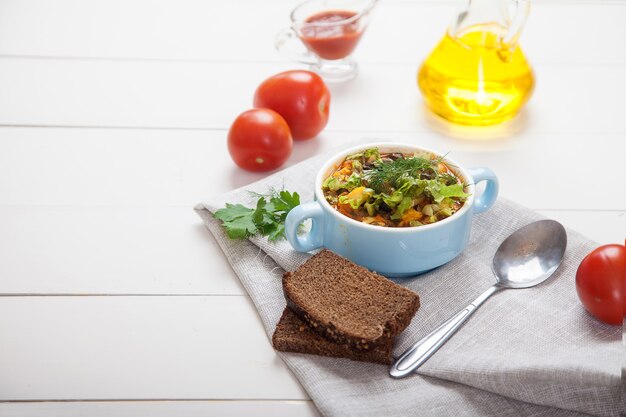 Bohnen-oliven-suppe mit kräutern in einer keramikschale, tomaten, olivenöl und brot auf einem weißen holztisch.