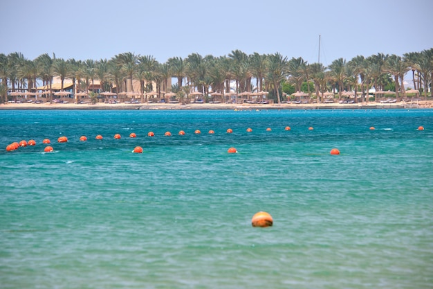 Boias amarelas flutuando na superfície do mar como marcador de restrição de natação em águas profundas em um resort tropical com vista da linha de costa à distância. Conceito de segurança de vida humana.