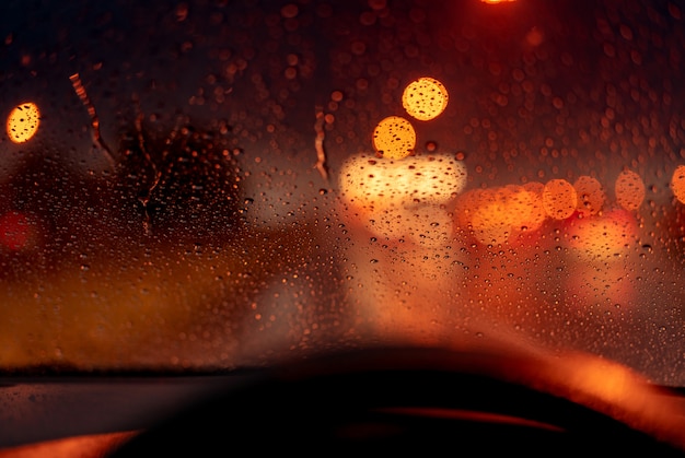 Bokeh alaranjado da luz da noite da luz de rua no dia do engarrafamento. Dia chuvoso. Janela de vidro transparente com gota de chuva. Clima romântico. Vida urbana.