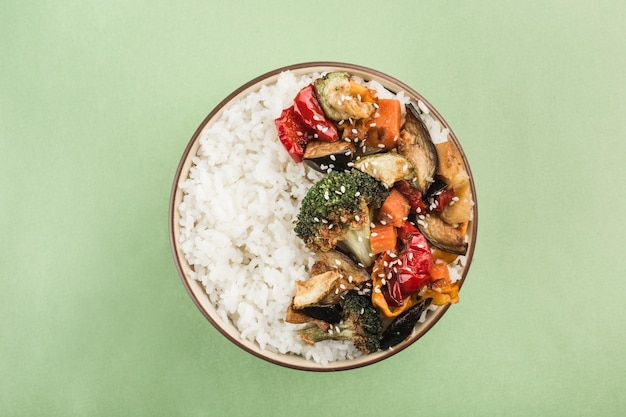 Un bol con arroz a la parrilla y verduras sobre un fondo verde claro. Comida asiática. Orientación horizontal. Vista superior.