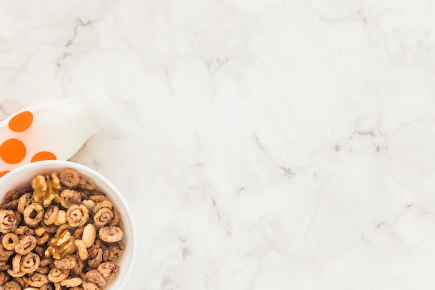 Foto bol con cereales y botella de leche blanca.