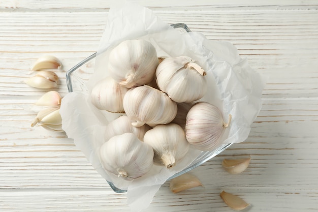 Bol de vidrio de bulbos de ajo fresco, rodajas en blanco de madera, vista superior. De cerca