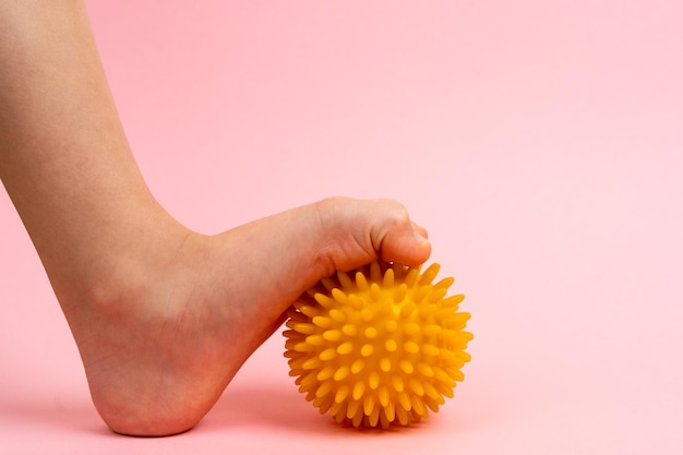 Bola de aguja amarilla para masajes y fisioterapia en un fondo rosa con el pie de un niño