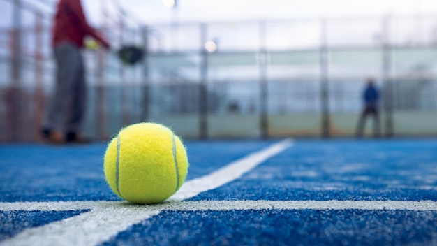 Bola amarela no chão atrás da rede de remo na quadra azul ao ar livre Homem que joga padel tênis Jogador caucasiano esportista batendo bolas Conceito de jogo de esporte de raquete