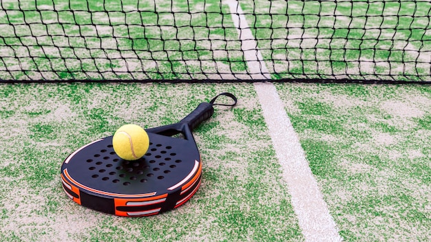 Bola amarela sobre a raquete de tênis padel atrás da rede na quadra verde ao ar livre