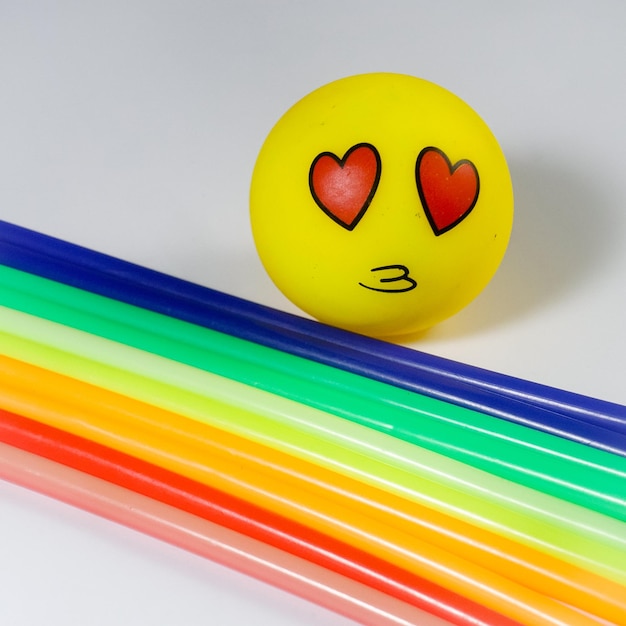 Foto una bola amarilla con un corazón rojo en los ojos está rodeada de popotes de colores del arco iris.