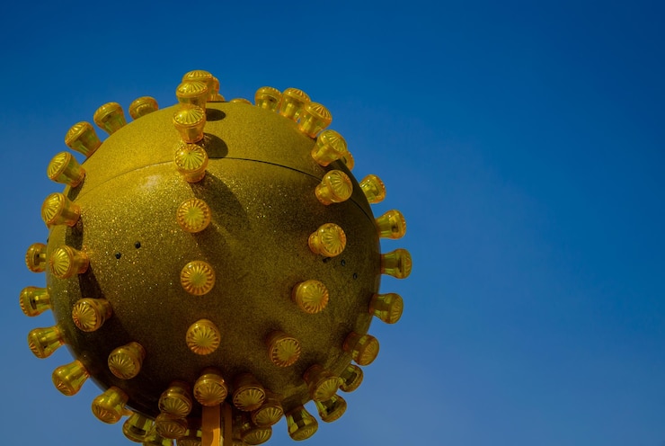 Foto una bola amarilla de coronavirus en un palo contra un cielo azul.