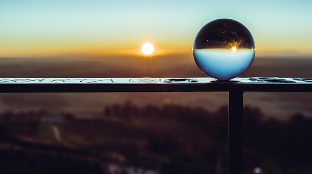Bola de cristal en la barandilla que refleja el cielo y el sol del amanecer