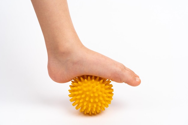 Bola de agulha amarela para massagem e fisioterapia em um fundo branco com pé de criança o conceito de prevenção e tratamento de pé valgo