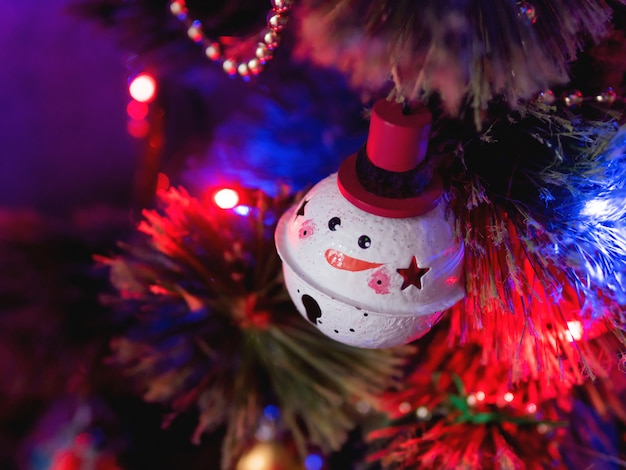 Bola de boneco de neve engraçado na árvore de Natal. Lâmpadas coloridas e decorações na árvore do abeto tradicional para a celebração do ano novo.