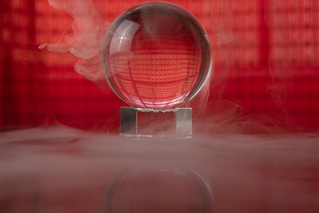 Bola de cristal refletindo um fundo vermelho e fumaça caindo, foco seletivo.