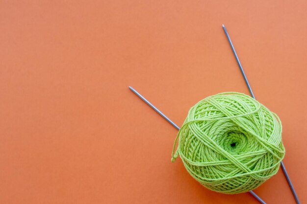 Bola de fio de tricô verde e agulhas de tricô vista superior em um fundo laranja com relaxamento de passatempos de espaço de cópia