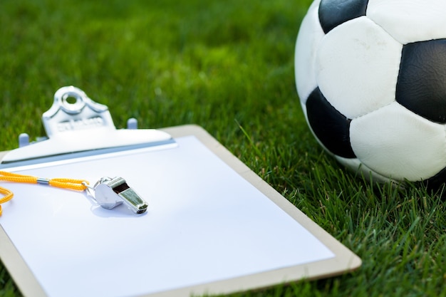 Foto bola de futebol com apito e prancheta na grama verde